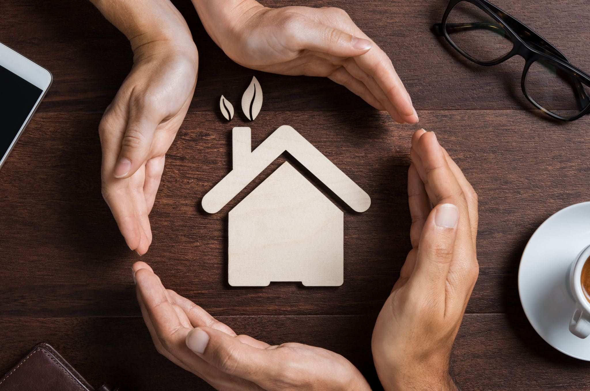 Top view of hands of a couple protecting their ecologigal house on wooden background. High angle view of hand of man and woman covering house shape. New home, Insurance and security concept.